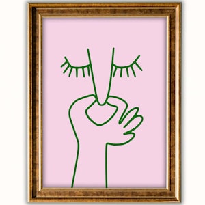 Puede incluir: Una impresión artística enmarcada con un dibujo lineal minimalista de una cara y una mano. La obra de arte es de color verde sobre un fondo rosa, dentro de un marco dorado. La imagen tiene una estética moderna y abstracta.