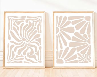 May include: Two rectangular wall art prints in light wooden frames. The left print features a beige abstract pattern of flowing, organic shapes on a white background. The right print displays a beige pattern of stylized flower petals on white.