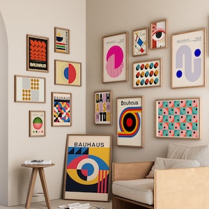 May include: A wall gallery featuring a collection of framed prints with geometric designs and the word "Bauhaus" in various colors and fonts. The prints are arranged in a grid pattern on a white wall.