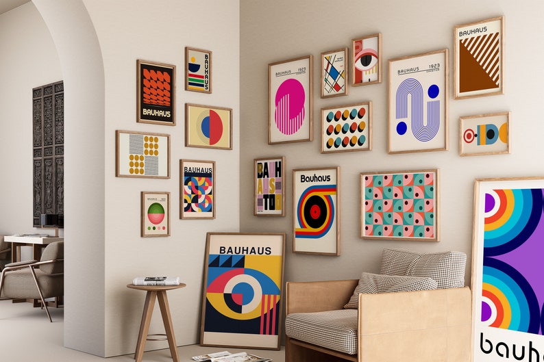 May include: A wall gallery featuring a collection of framed prints with geometric designs and the word "Bauhaus" in various colors and fonts. The prints are arranged in a grid pattern on a white wall.