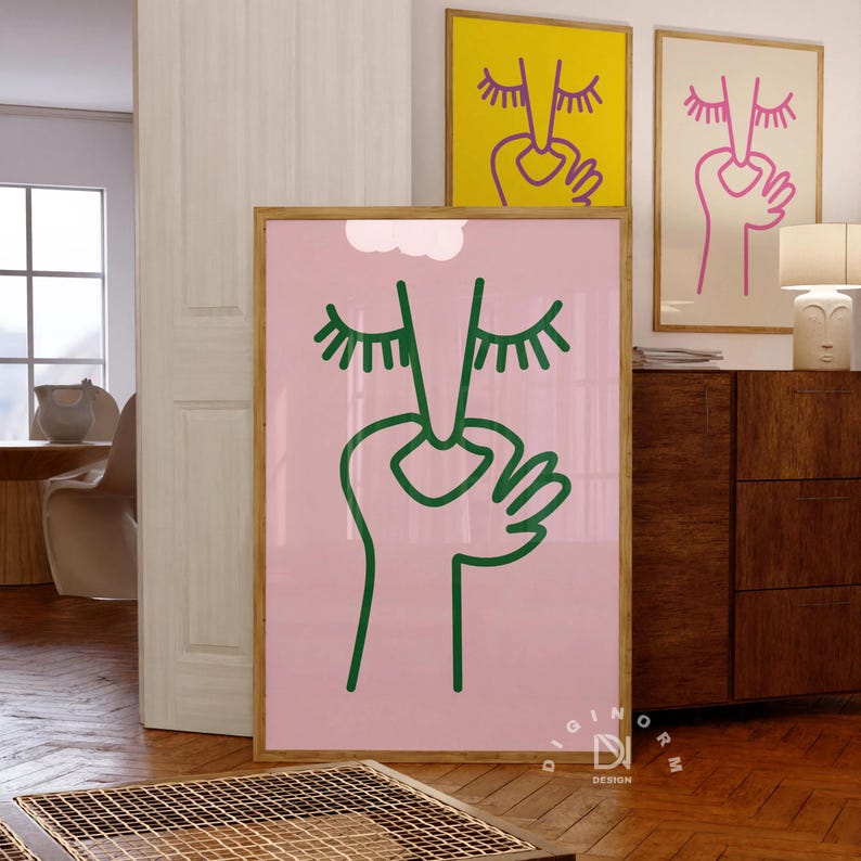 May include: A pink poster with a green line drawing of a face with closed eyes and a hand covering the mouth. The poster is framed in wood and is hanging on a wall. The text 'DIGINORM DESIGN' is printed in white on a black background at the bottom of the poster.