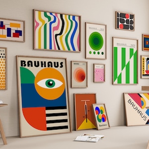 May include: A collection of framed Bauhaus-style posters with geometric shapes and patterns in various colors, including red, yellow, green, blue, and black. The posters are arranged on a white wall with wooden frames.