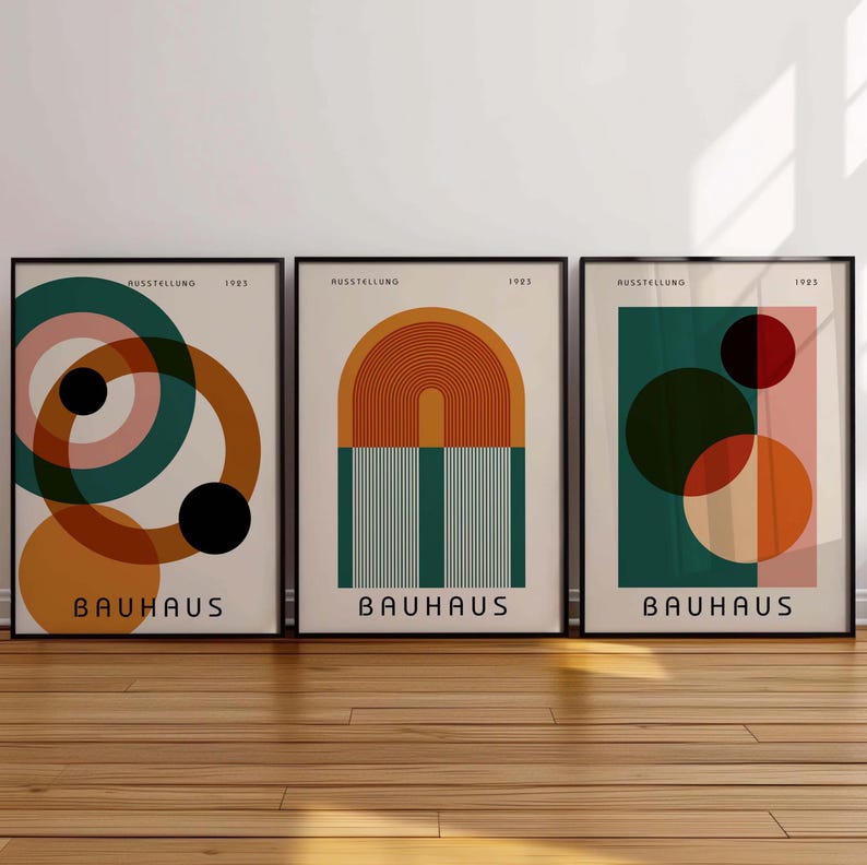K&ouml;nnte beinhalten: Drei Bauhaus-Kunstdrucke mit geometrischen Formen in Orange-, Rot-, Gr&uuml;n- und Rosat&ouml;nen. Die Drucke zeigen den Text "AUSSTELLUNG 1923" und "BAUHAUS".