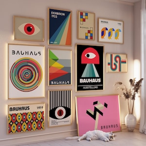 May include: A gallery wall of framed prints featuring geometric designs and the word "Bauhaus" in various fonts and colors. The prints are arranged in a grid pattern on a white wall.