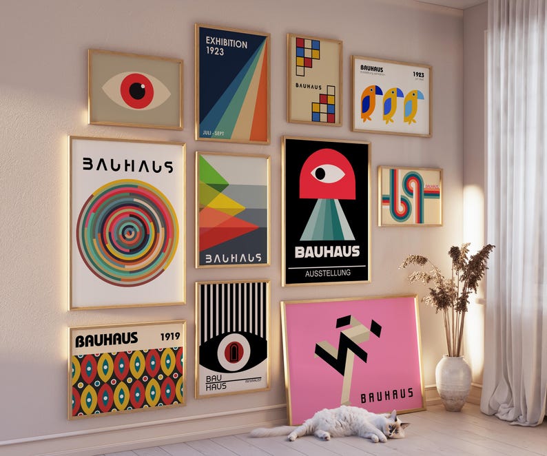May include: A gallery wall of framed prints featuring geometric designs and the word "Bauhaus" in various fonts and colors. The prints are arranged in a grid pattern on a white wall.