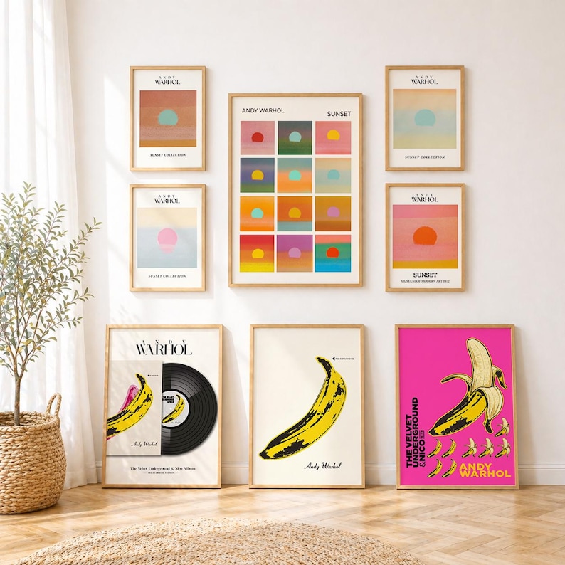 May include: A gallery wall featuring eight framed Andy Warhol prints. The collection includes four sunset-themed prints, one large grid print titled Sunset, one vinyl record cover print, and two banana-themed prints on white and bright pink backgrounds.