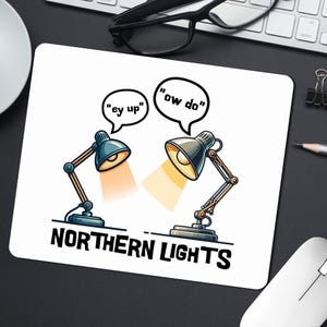 May include: White mousepad featuring a cartoon design of two desk lamps with speech bubbles saying "ey up" and "ow do". The text "NORTHERN LIGHTS" is printed below the lamps, a reference to the Northern Lights.