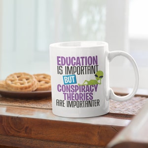 May include: White ceramic mug with a green alien graphic and the text "Education is important but conspiracy theories are importanter".