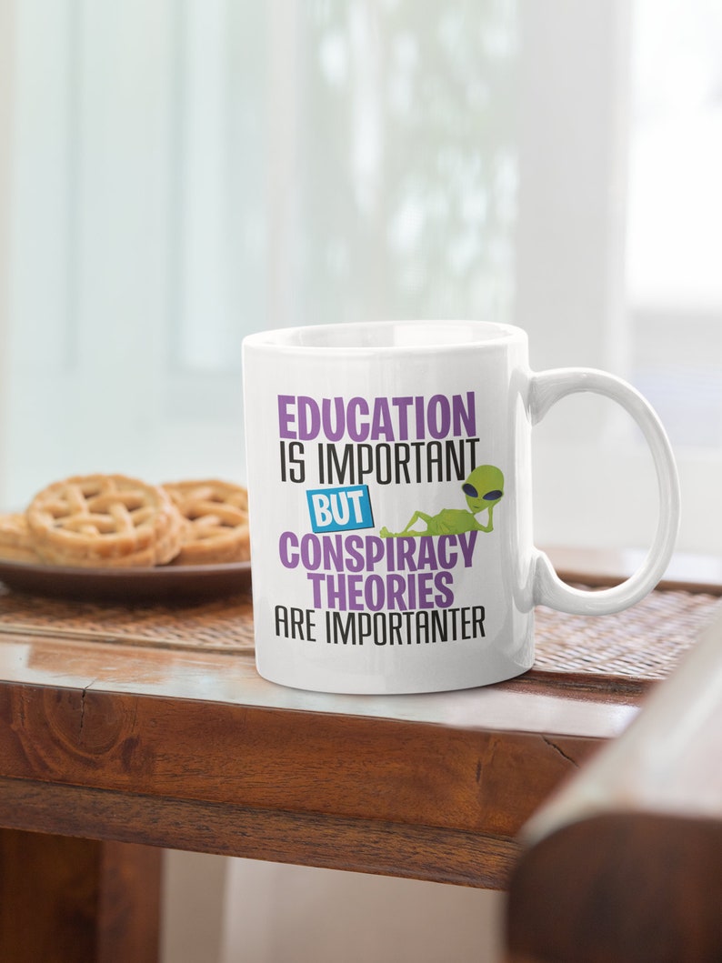 May include: White ceramic mug with a green alien graphic and the text "Education is important but conspiracy theories are importanter".