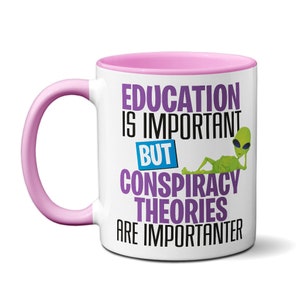 May include: White ceramic coffee mug with a pink rim and handle. The mug has a purple design that says "Education is important but conspiracy theories are importanter". A green alien with sunglasses is lying on the mug.