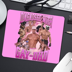 May include: Rectangular pink mousepad with a collage of shirtless men and the text "DIAGNOSED WITH GAY-DHD". The mousepad is on a black surface, with a keyboard and mouse in view. The text is in a stylized font.