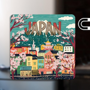 May include: A square magnet featuring a colorful illustration of a Japanese cityscape. The design includes buildings, cherry blossom trees, and the word "JAPAN" in large letters. A mountain is visible in the background. A magnet symbol is on the right.