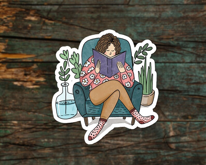 Puede incluir: Una mujer sentada en un sill&oacute;n de color verde azulado leyendo un libro morado. Lleva una camisa rosa con flores blancas y tiene el pelo casta&ntilde;o. Hay dos plantas en macetas en la habitaci&oacute;n.