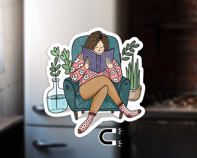 Puede incluir: Una mujer se sienta en un sill&oacute;n de color turquesa leyendo un libro. Lleva una camisa de flores rosa y blanca y tiene el pelo casta&ntilde;o. El sill&oacute;n est&aacute; decorado con un patr&oacute;n floral y hay plantas en macetas a ambos lados del sill&oacute;n.