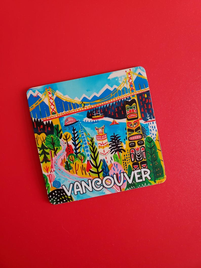 Op de afbeelding: Een kleurrijke vierkante magneet met een gestileerde illustratie van Vancouver, Canada. Het ontwerp omvat een brug, een totempaal en de naam van de stad in witte letters tegen een levendig landschap van blauw, groen en geel.