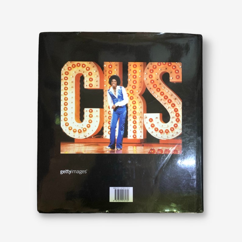 K&ouml;nnte beinhalten: Ein schwarzer Buchumschlag mit einem Foto eines Mannes in einem blauen Overall, der vor einem gro&szlig;en, beleuchteten Schild steht, auf dem "CKS" steht. Der Buchumschlag enth&auml;lt auch den Text "gettyimages" und einen Barcode.