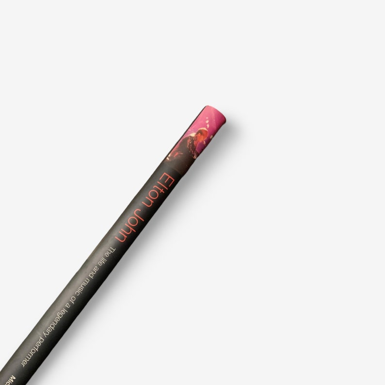 May include: A rolled-up poster featuring a photo of Elton John, a legendary performer. The poster is black with orange text that reads "Elton John The life and music of a legendary performer".