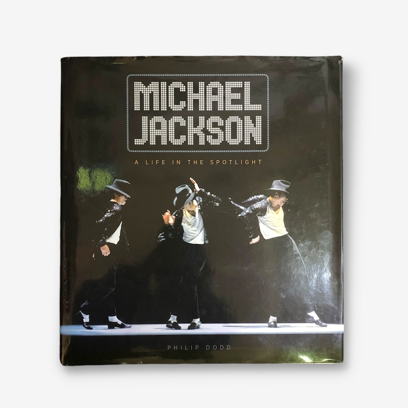 K&ouml;nnte beinhalten: Ein schwarzes Hardcover-Buch mit dem Titel "MICHAEL JACKSON A LIFE IN THE SPOTLIGHT" in wei&szlig;en Buchstaben. Der Umschlag zeigt ein Foto von Michael Jackson, der in einem schwarzen Anzug und wei&szlig;em Hemd auf der B&uuml;hne auftritt.