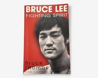 May include: A red book cover with the title "Bruce Lee Fighting Spirit" in white text. A black and white photo of Bruce Lee is featured on the cover. The book is by Bruce Thomas and is a new edition.
