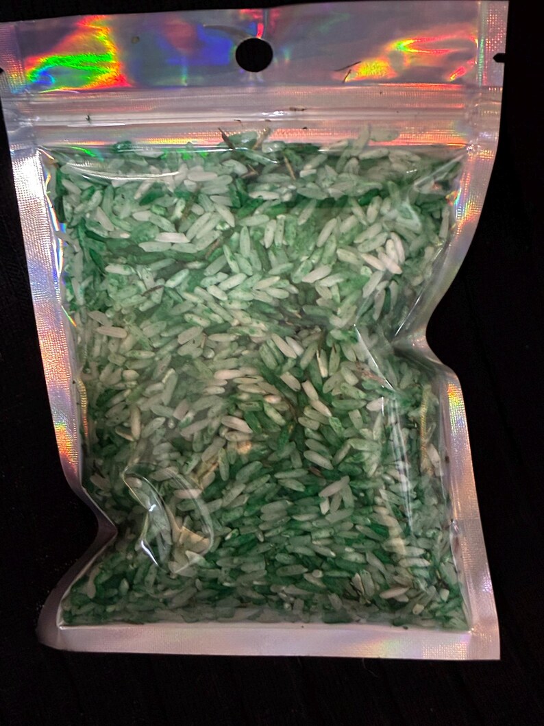 May include: A clear, holographic-edged resealable plastic pouch filled with a mixture of white and various shades of green dyed rice grains. The bag features a top hanging hole and a zip-lock closure, containing a loose collection of small, elongated, dried food-grade rice kernels.