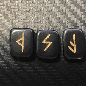 May include: Three black stone runes with gold inscriptions. The runes are arranged in a row from left to right. The runes are "Algiz", "Sowulo", and "Eihwaz".