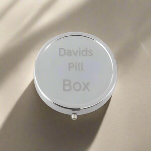 May include: A silver round pill box with the text "Davids Pill Box" engraved on the lid.