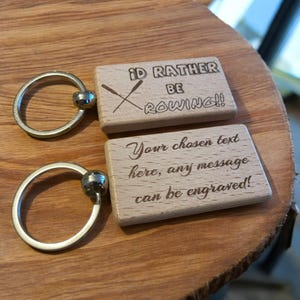 May include: Two wooden keyrings with a silver ring. The top keyring has the text "I'd rather be rowing!" with a pair of crossed oars. The bottom keyring has the text "Your chosen text here, any message can be engraved!"