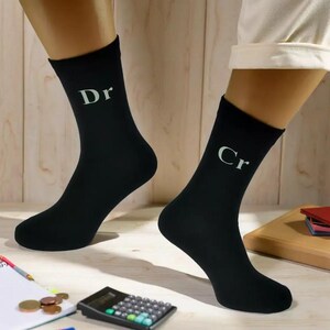 May include: A pair of black socks, one with the letters "Dr" and the other with "Cr" printed in white. The socks are being worn. A calculator, notepad, and coins are in the background.