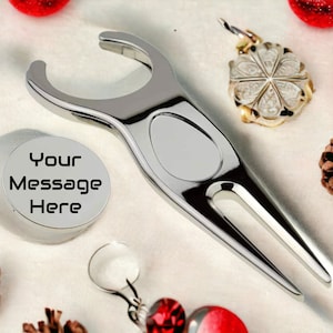 May include: A silver golf ball retriever with a personalised disc that says "Your Message Here". The retriever has a fork-like end and a loop handle. The disc is round and has a smooth surface.