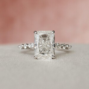May include: A silver engagement ring featuring a large, clear, square-shaped diamond. The band is set with smaller diamonds.