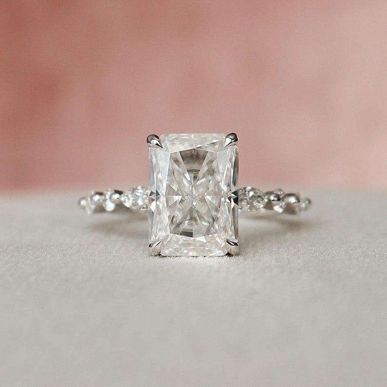 May include: A silver engagement ring featuring a large, clear, square-shaped diamond. The band is set with smaller diamonds.