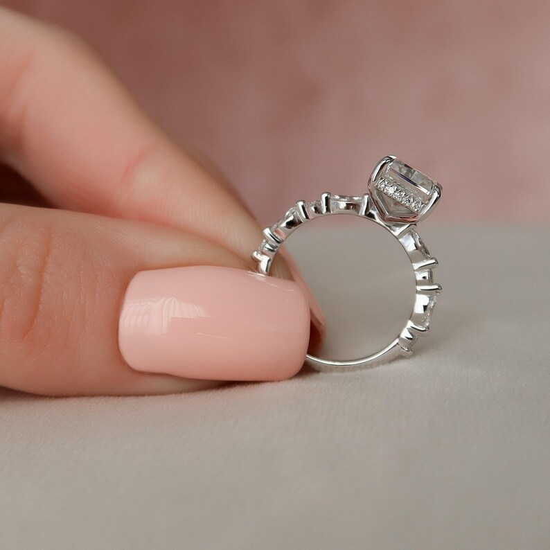 May include: A silver ring featuring a large, clear, square-shaped gemstone surrounded by smaller diamonds. The ring has a delicate, intricate design.