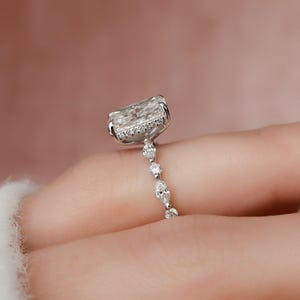 May include: A silver engagement ring featuring a large, square-shaped diamond set in a pave setting. The band is embellished with smaller diamonds in a delicate, pear-shaped design.
