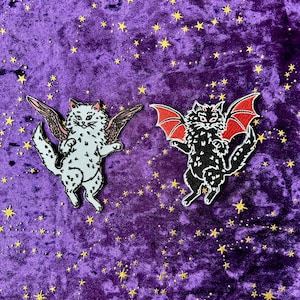 May include: Two embroidered patches featuring cat designs with wings. One cat is white with black spots and brown wings, the other is black with red bat wings. The background is a purple velvet fabric with gold star accents.