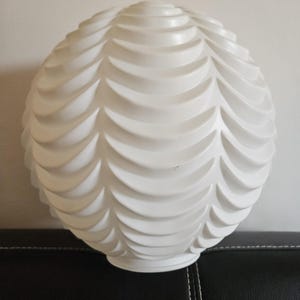 May include: A spherical white glass lamp shade featuring a repeating moulded pattern of overlapping, curved, scale-like ridges that wrap around the entire surface, terminating in a circular opening at the base for a light fixture attachment.