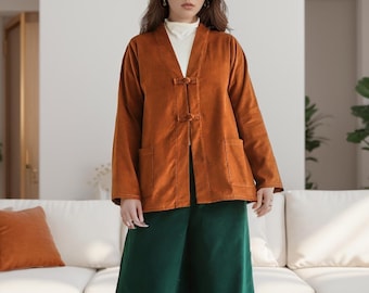 Könnte beinhalten: Ein Outfit mit einer rostfarbenen Cordjacke mit zwei Vordertaschen und Knebelverschlüssen, kombiniert mit einer Hose mit weitem Bein aus smaragdgrünem Cord. Das Ensemble wird durch cremefarbene Schuhe ergänzt.