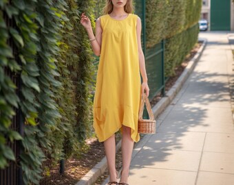 Peut inclure: Une femme portant une robe jaune sans manches et tenant un panier en osier. Elle se tient sur un trottoir avec des buissons verts en arrière-plan.