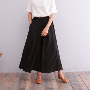 May include: A woman is wearing a white short-sleeved shirt and black wide-leg pants. The pants have a wide, flowing silhouette and a high waist.