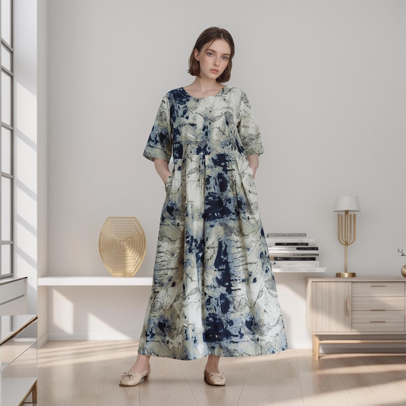 May include: A long, flowing dress with a blue and white abstract print. The dress has a round neckline and three-quarter sleeves. The model is wearing the dress with a pair of flat shoes.