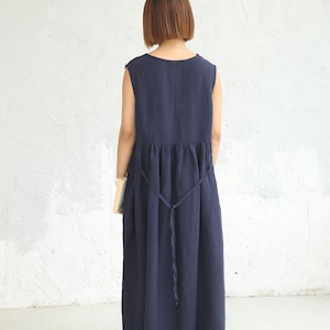 May include: A navy blue sleeveless maxi dress with a gathered waist and a tie belt. The dress is made of a lightweight fabric and has a relaxed fit.