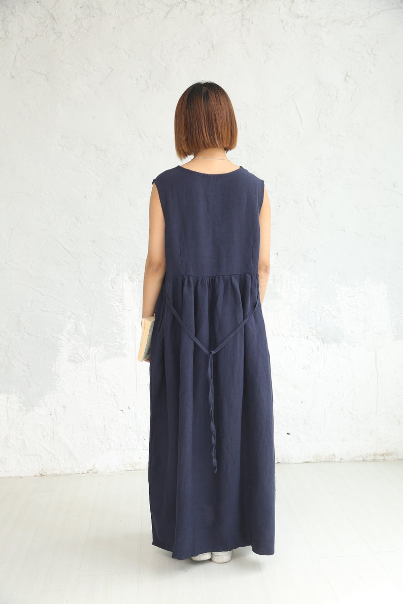 May include: A navy blue sleeveless maxi dress with a gathered waist and a tie belt. The dress is made of a lightweight fabric and has a relaxed fit.