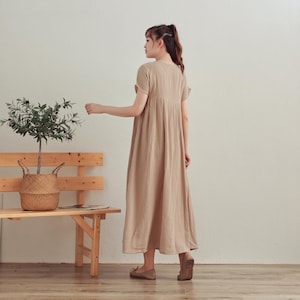 Puede incluir: Un vestido maxi beige con mangas cortas y escote en V. El vestido tiene una falda plisada y un corte holgado.