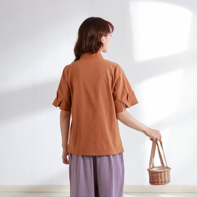 Pode incluir: Uma mulher vestindo uma camisa marrom de manga curta e cal&ccedil;as roxas est&aacute; segurando uma pequena cesta de vime com uma al&ccedil;a branca.