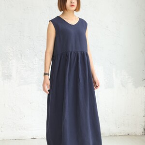 May include: A navy blue sleeveless maxi dress with a gathered waistline. The dress is made of a lightweight fabric and has a relaxed fit.