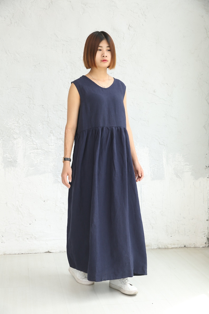 May include: A navy blue sleeveless maxi dress with a gathered waistline. The dress is made of a lightweight fabric and has a relaxed fit.