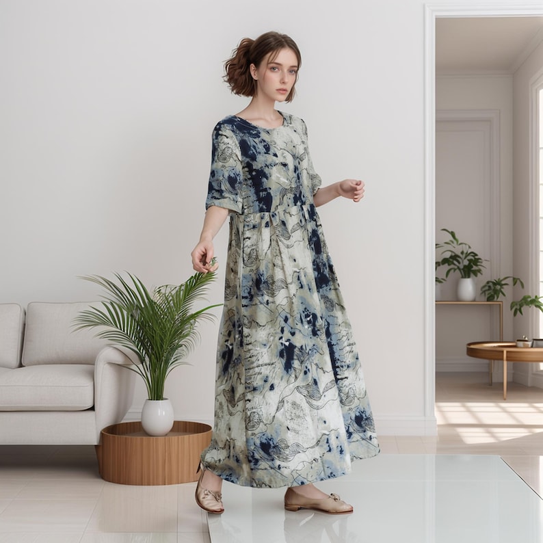 May include: A woman wearing a long, flowing dress with a blue and white abstract print. The dress has a round neckline and three-quarter sleeves. She is standing on a white floor with a plant and a sofa in the background.