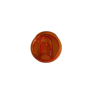 Op de afbeelding: Een oranje plastic tumblerdeksel met een schuifsluiting. Het deksel is cirkelvormig met een verzonken midden en een klein lipje om de schuif te openen en te sluiten. Het plastic is doorschijnend.