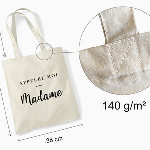 Może przedstawiać: Kremowa torba typu tote z czarnym napisem "Appelez Moi Madame". Torba ma 42 cm wysokości, 38 cm szerokości i uchwyty o długości 34 cm. Gramatura materiału wynosi 140 g/m2.