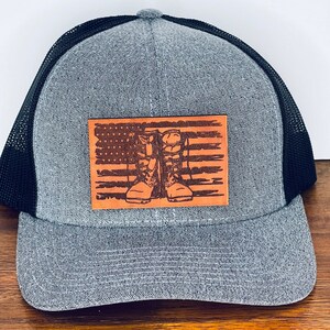 May include: A gray and black trucker hat with a brown leather patch featuring a distressed American flag and a pair of boots.