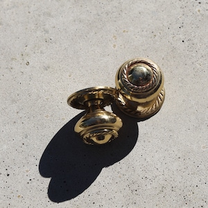 May include: Two gold door knobs with a rope design. The knobs are on a light grey surface.